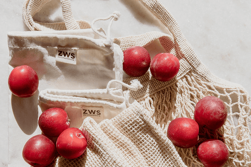 red plums scattered around various types of resusable cotton bags