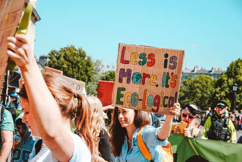 A woman in a crowd holding a sign that says ‘‘less is more. It’s Eco-logical’’.