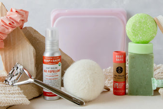 Arrangement of silver safety razor, bug spray, wool dryer ball, pink silicone bag, and soap bars