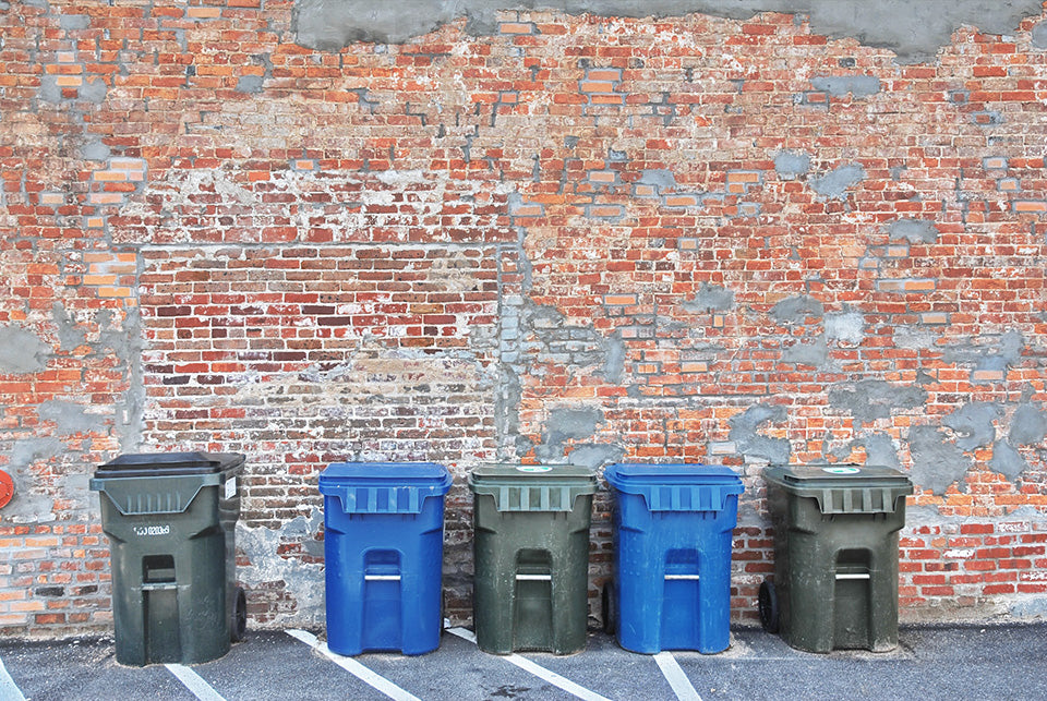 black and blue garbage bins lined up against a red brick wall