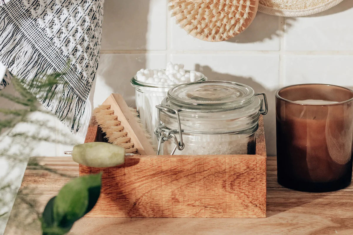 sustainable bathroom accessories, like wood organizational boxes, glass jars, plastic-free brushes, and soy candles