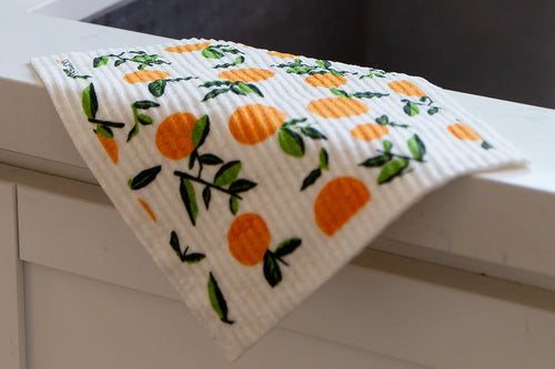 a sponge cloth with a tangerine print on the front draped over the front ledge of a kitchen sink