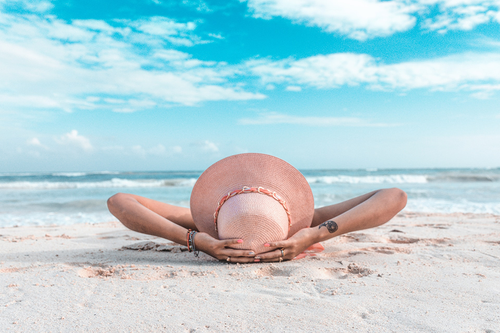 woman in tan sun hat lying on a sandy beach during the day