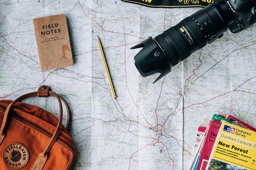 flat lay of notebook, backpack, travel guides, and camera on top of a paper map