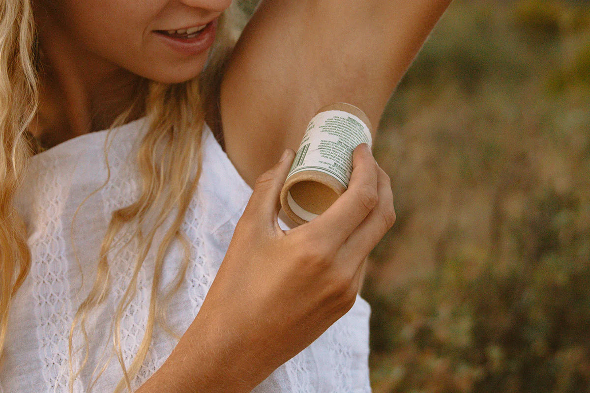 A young blonde woman putting deodorant on her armpit