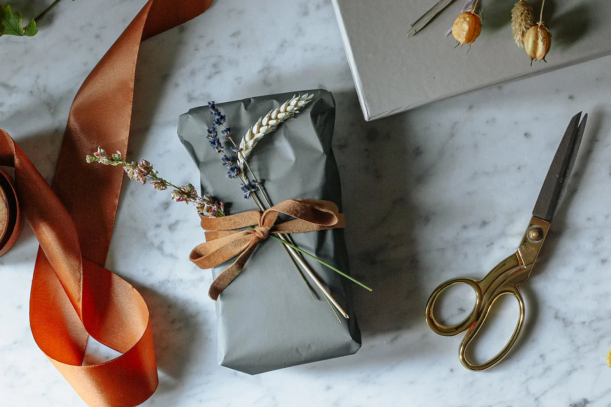 A small gift wrapped in gray paper and brown ribbon with a few dried flowers tucked in the bow