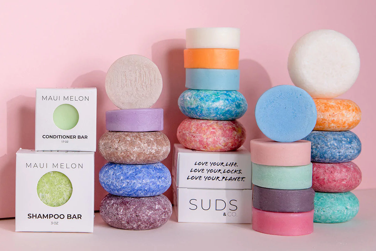 SUDS & Co. shampoo and conditioner bars stacked in columns on a pink background