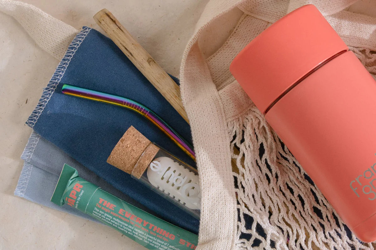 a bundle of low waste summer essentials, including paper packaged balm, a compact water filter, stainless steel straw, reusable paper towels, and reusable coffee cup